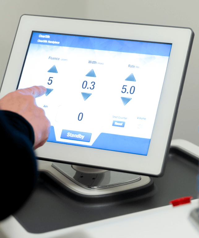 A close-up of a touchscreen medical device interface showing adjustable settings, with a person’s hand pointing at the screen to change parameters.