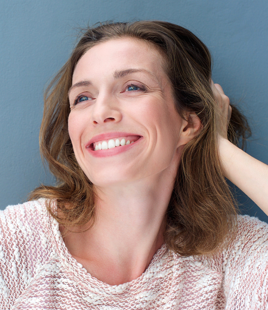 Smiling woman with shoulder-length brown hair wearing a light knit top, looking upward with a joyful expression.