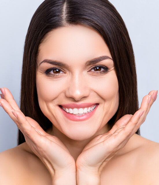 Smiling woman with straight dark hair holding her face in her hands, showcasing smooth, radiant skin.