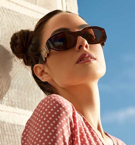 Woman with a bun in hair and sunglasses leaning against a wall
