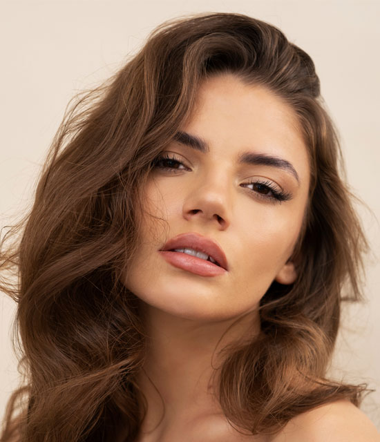 Close-up of a woman with voluminous wavy brown hair and a soft, confident expression.