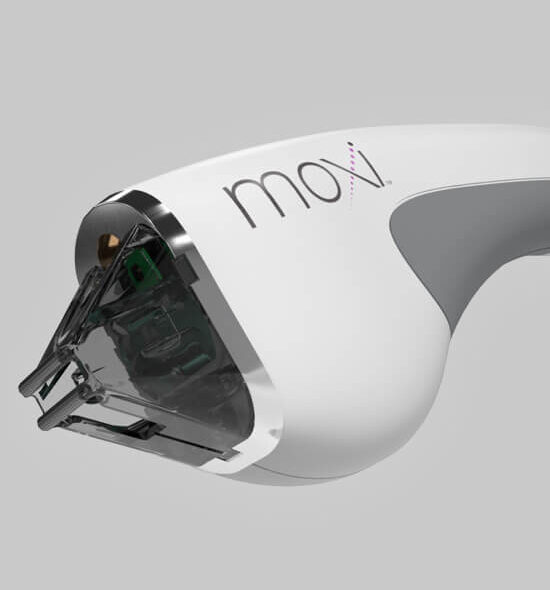 A close-up of a Moxi laser handpiece, a sleek white cosmetic dermatology device with a transparent treatment tip, shown against a plain grey background.