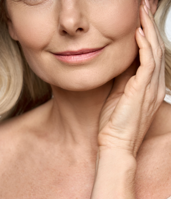 Close-up of middle-aged woman with smooth skin, subtle smile, and hand gently touching face and neck