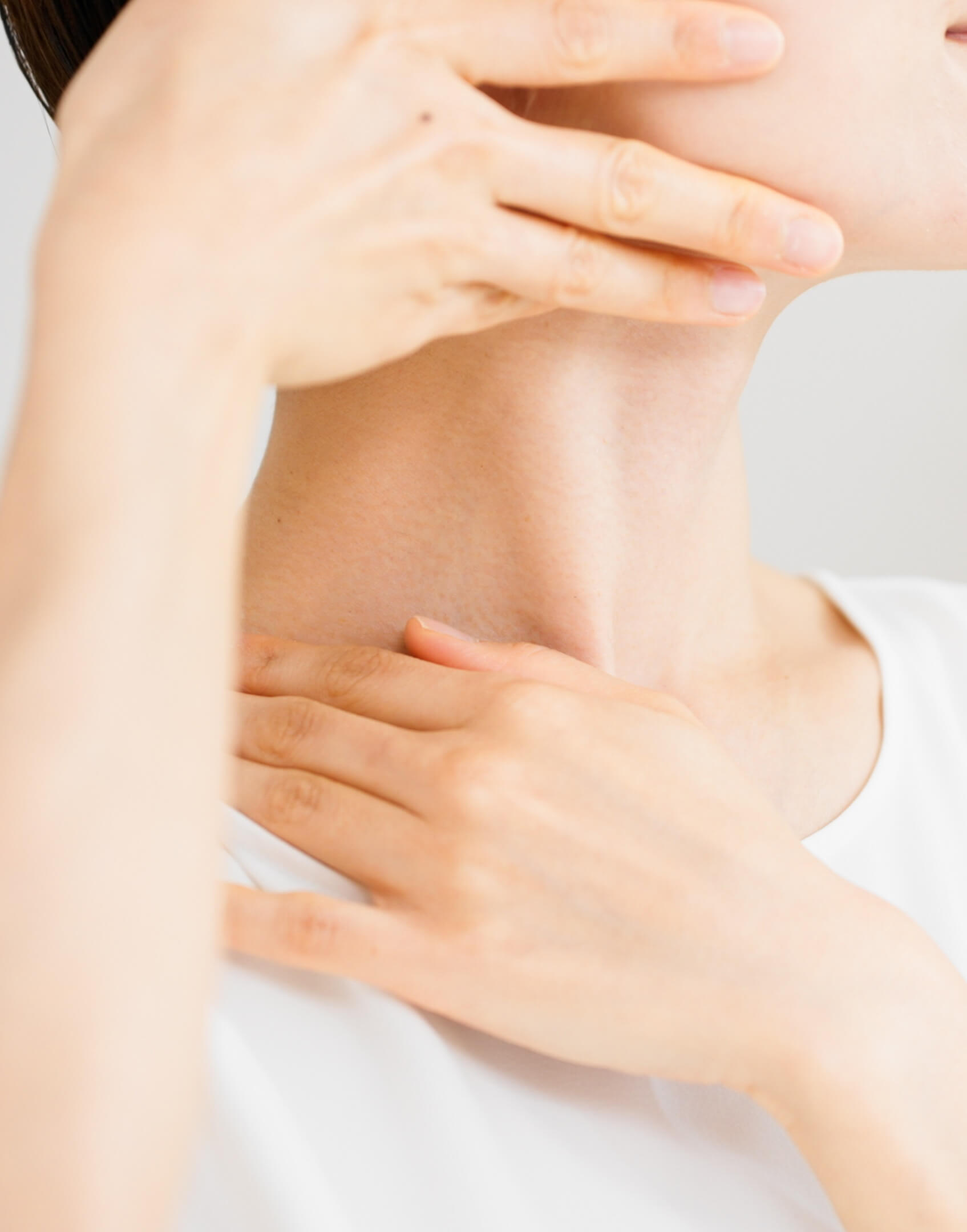 Close-up of a person touching their neck and collarbone area with both hands, wearing a white top.