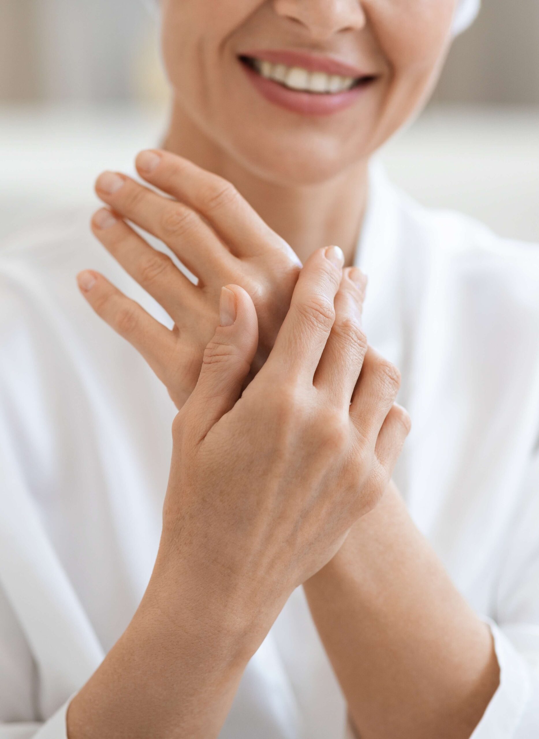 Close-up of a smiling woman gently touching and examining the skin on her hands.