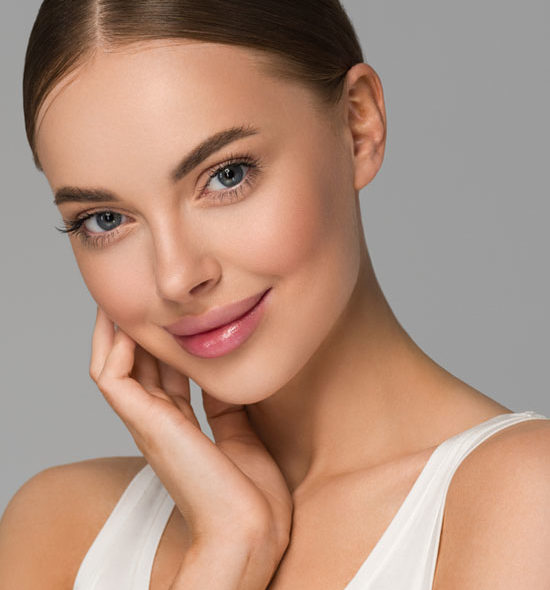 Young woman with clear glowing skin, soft smile, and hand gently touching her face against a neutral background