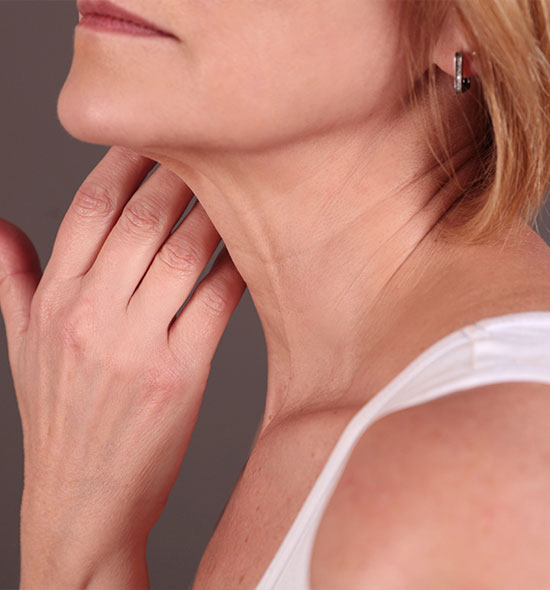 Close-up of a middle-aged woman’s lower face and neck, showing skin texture and early signs of aging while gently touching her neck