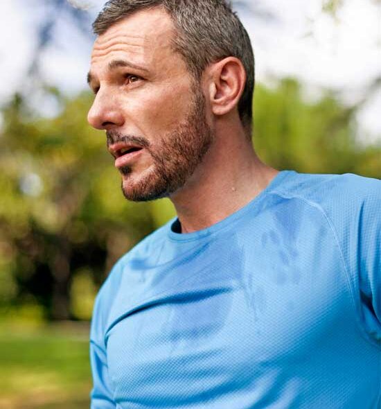 Middle-aged man with short hair and a beard wearing a blue athletic shirt, appearing thoughtful outdoors after exercise.