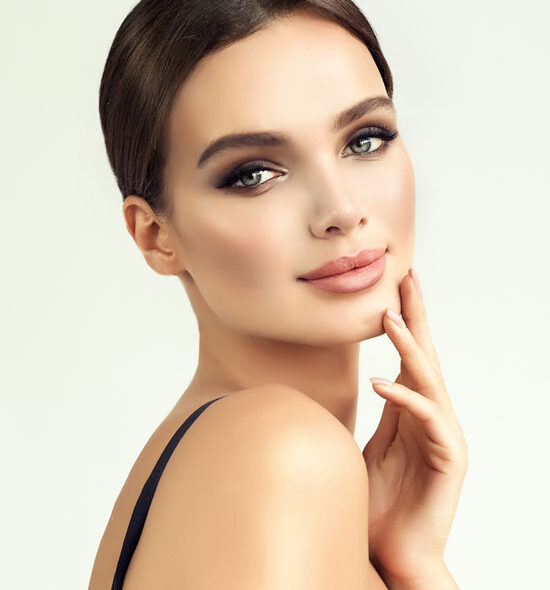 Up close portrait of a woman after a lip filler treatment with flawless skin, neutral-toned makeup,a soft smile, and full lips, gently touching her face.