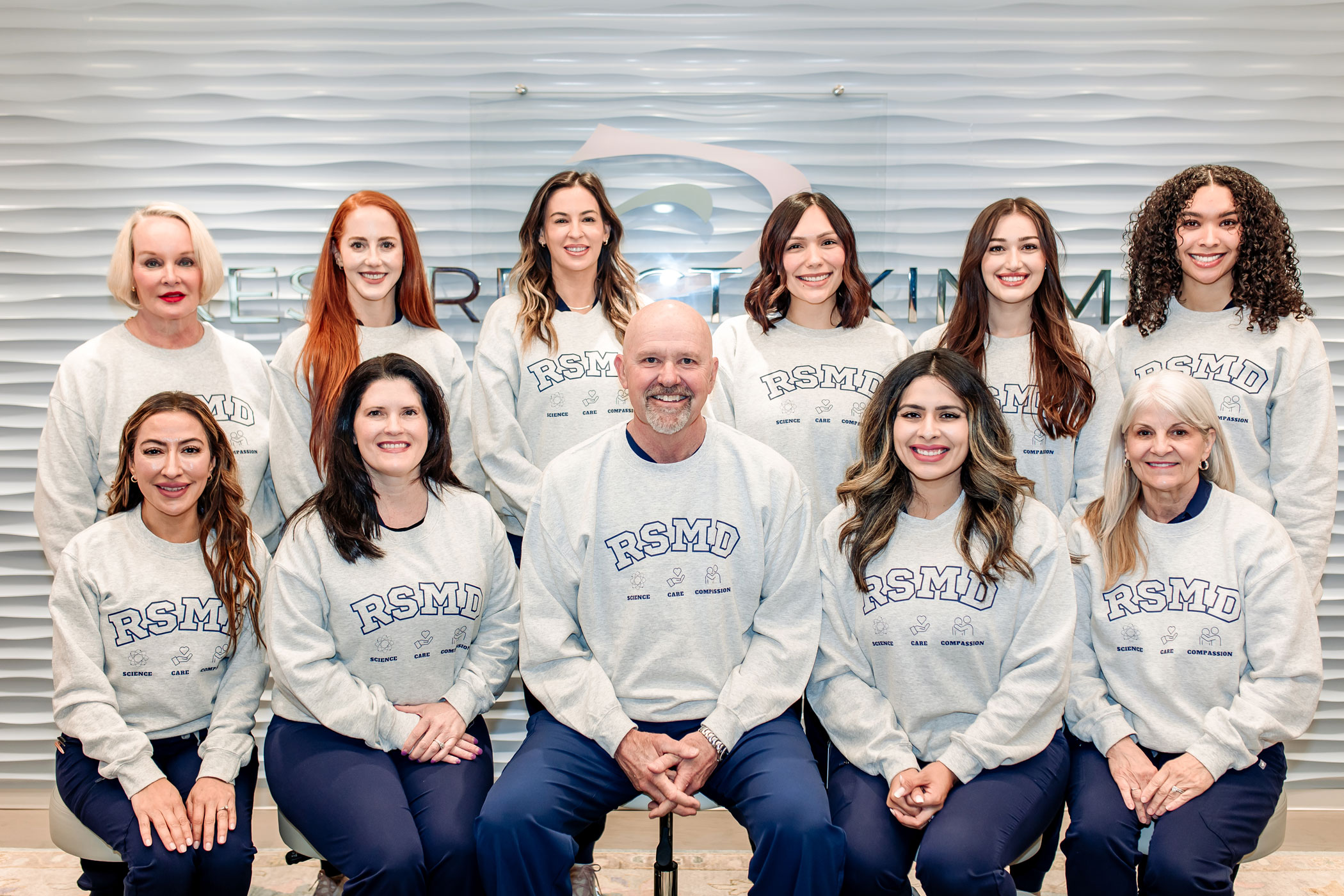 Group photo of the Resurrect Skin MD team wearing matching RSMD sweatshirts, smiling together in the clinic reception area