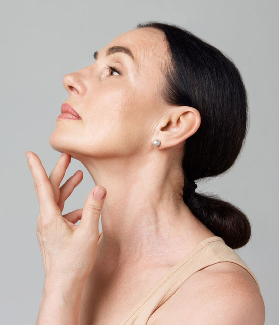 Woman with smooth skin tilting her head upward and touching her neck, showcasing a defined jawline.