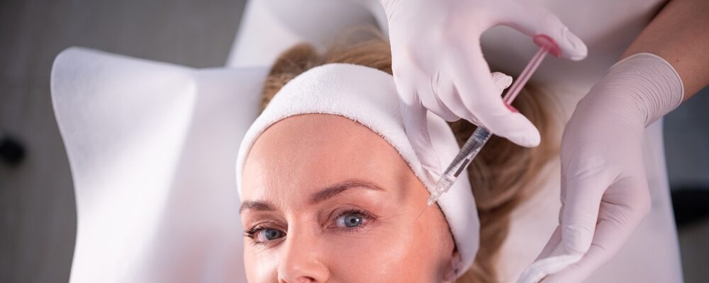 Woman receiving a minimally invasive facial treatment injection at a medical aesthetics clinic, promoting skin rejuvenation and anti-aging results.