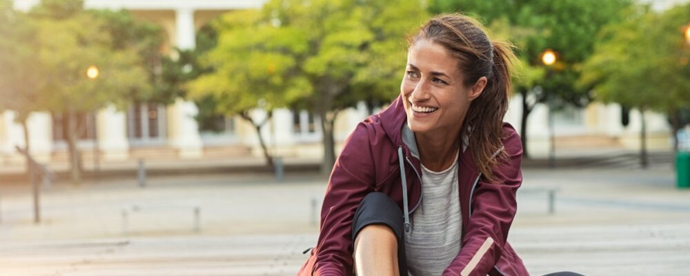 Woman in running clothes smiling and adjusting her shoe